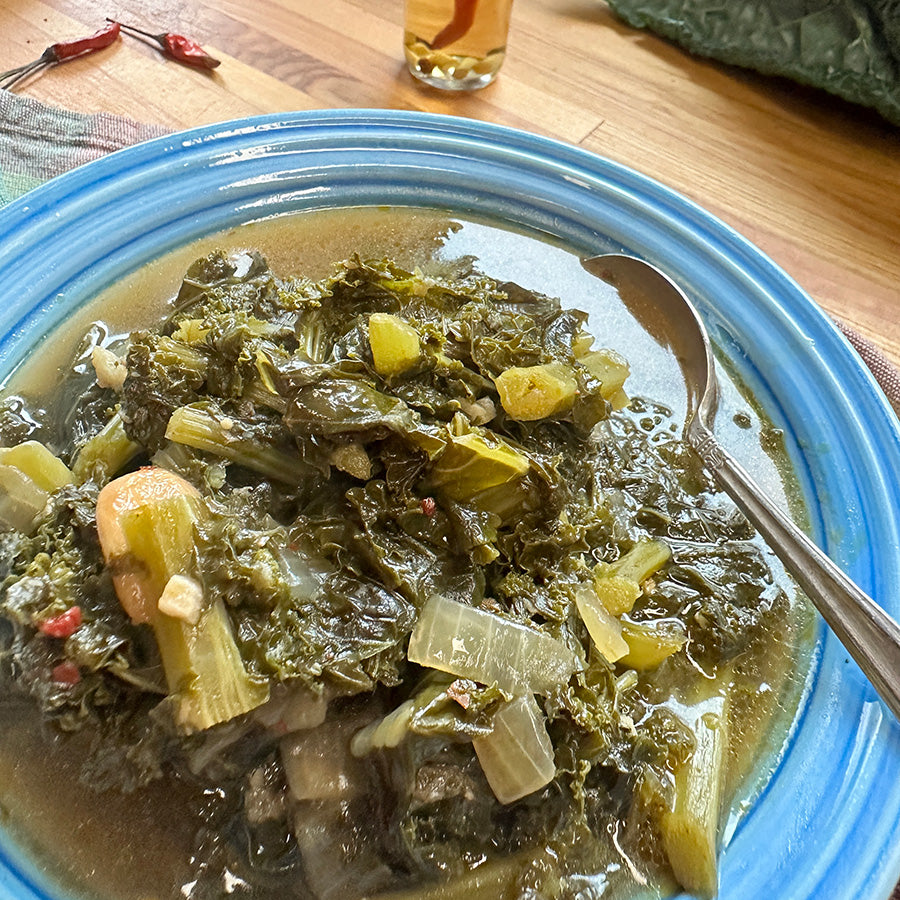 Blue bowl of braised greens with a spoon on a wooden table