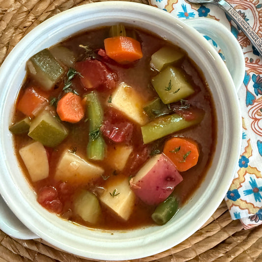 Vegetable soup in a white bowl on a woven mat with a floral-patterned napkin and spoon.
