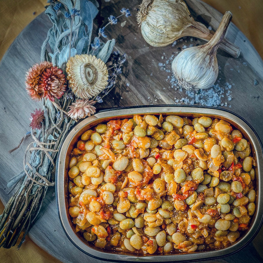 Baked dish with butter beans and on a wooden board with garlic and flowers.