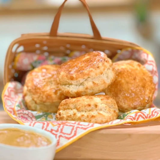 Biscuits in a woven basket with a bowl of honey butter on a wooden surface