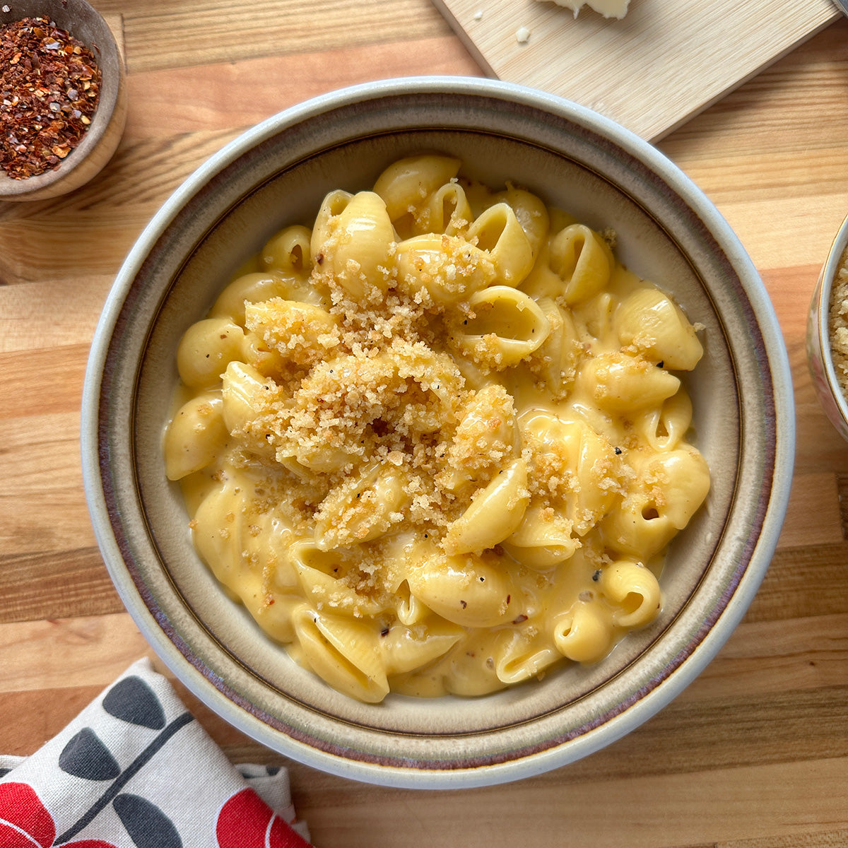 Bowl of macaroni and cheese with breadcrumbs on a wooden table