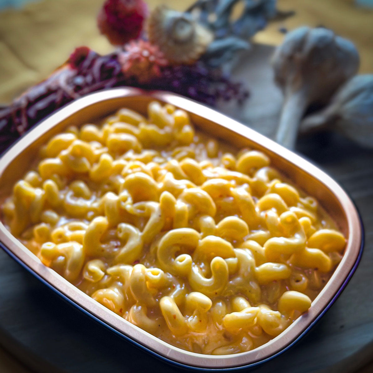 Macaroni and cheese in a takeout container on a table with decorative items.