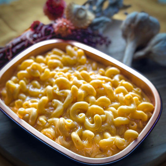 Macaroni and cheese in a takeout container on a table with decorative items.