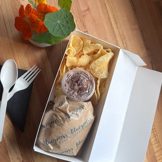 Takeout box with chips, a drink, and chips on a wooden table.