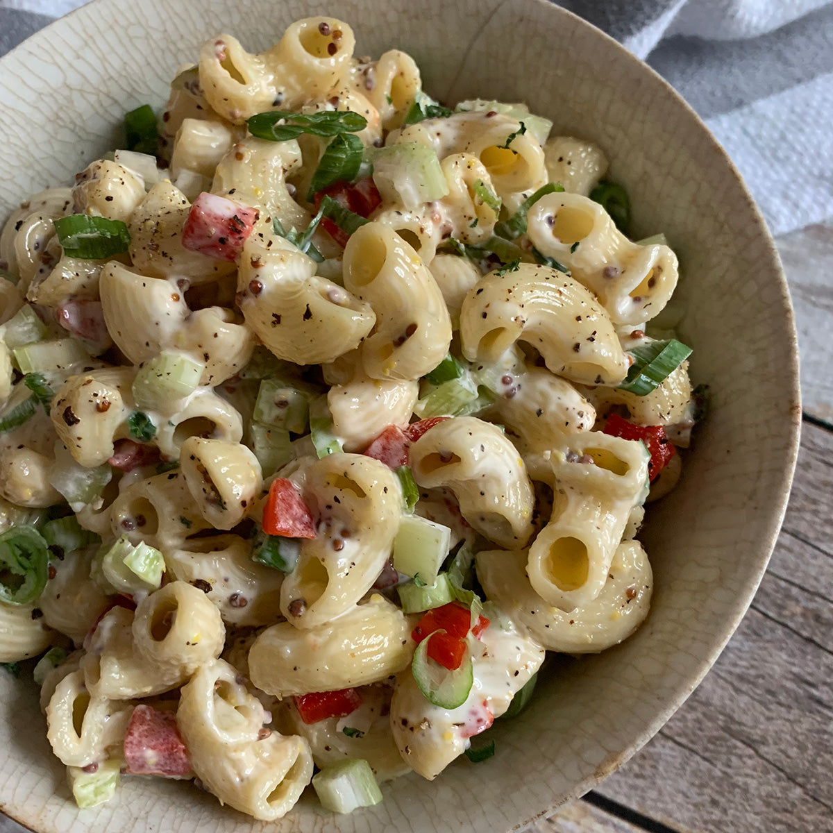 Pasta salad with vegetables in a beige bowl on a wooden surface